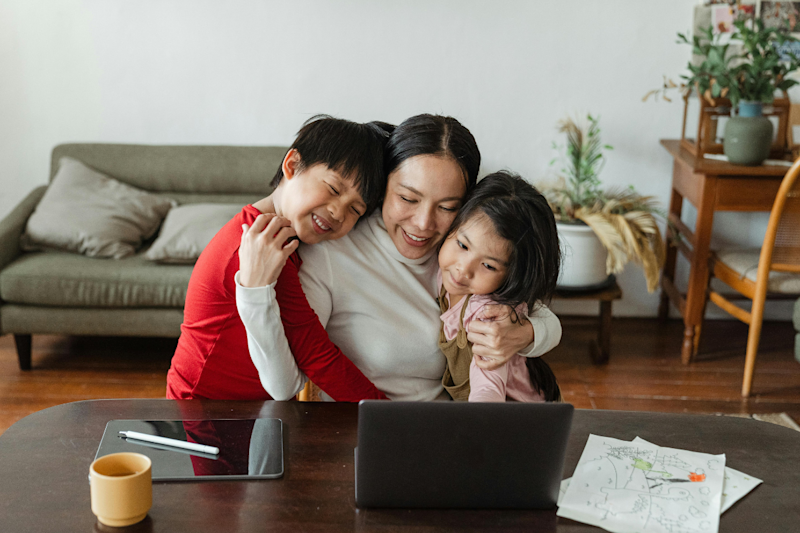 A mother hugging her son and daughter in her living room.