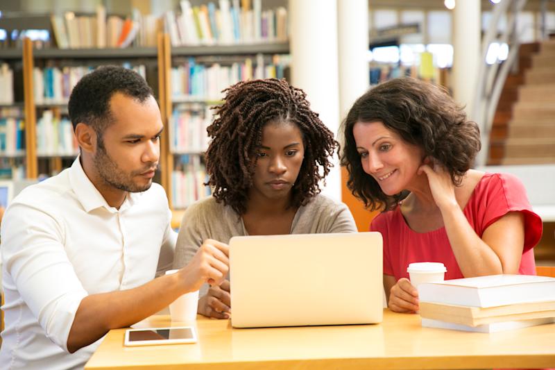Front view of tired mature students looking at laptop. Thoughtful man and women sitting at table with modern devices. Education concept