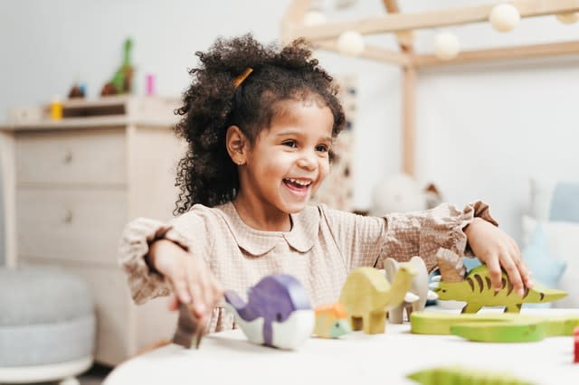 A child happily playing with wooden animals, not looking at the camera.