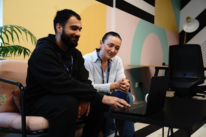 Two Anna Freud students, smiling and looking at a laptop.