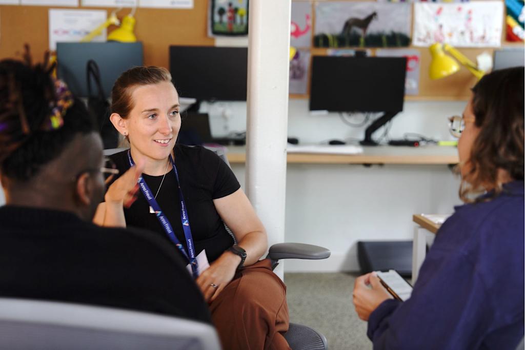 Three Anna Freud staff in training, with a woman in the middle in focus during conversation. Two people in the foreground are out of focus with their backs to the camera.