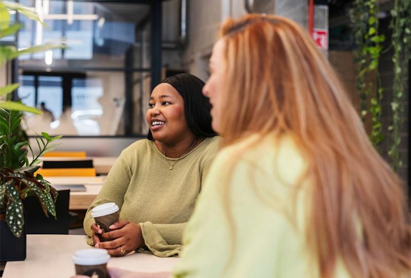 A photograph of two young women smiling and drinking coffee.