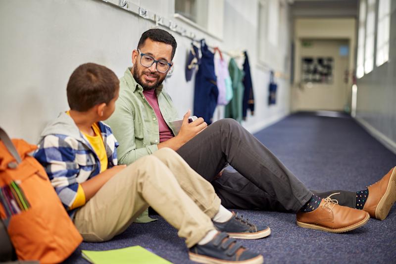 Man sitting on the floor of a corridor, smiling down at a young boy sitting beside him.