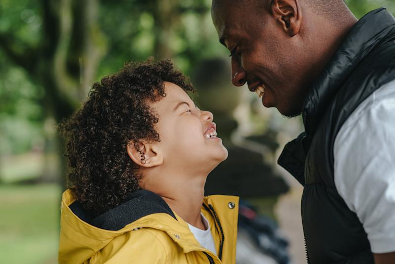 Man and boy broadly smiling at each other outside. Profile view.
