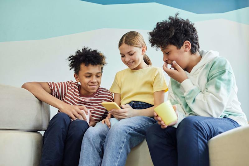 Three young people seated looking at a phone.