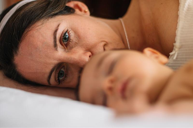 Mom with tired face and lost look, next to her baby as she sleeps.