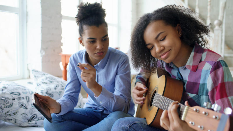 Two young women playing guitar and holding a tablet