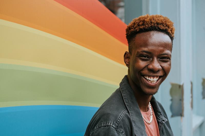 very smiling person looking at camera with rainbow coloured stripes in background