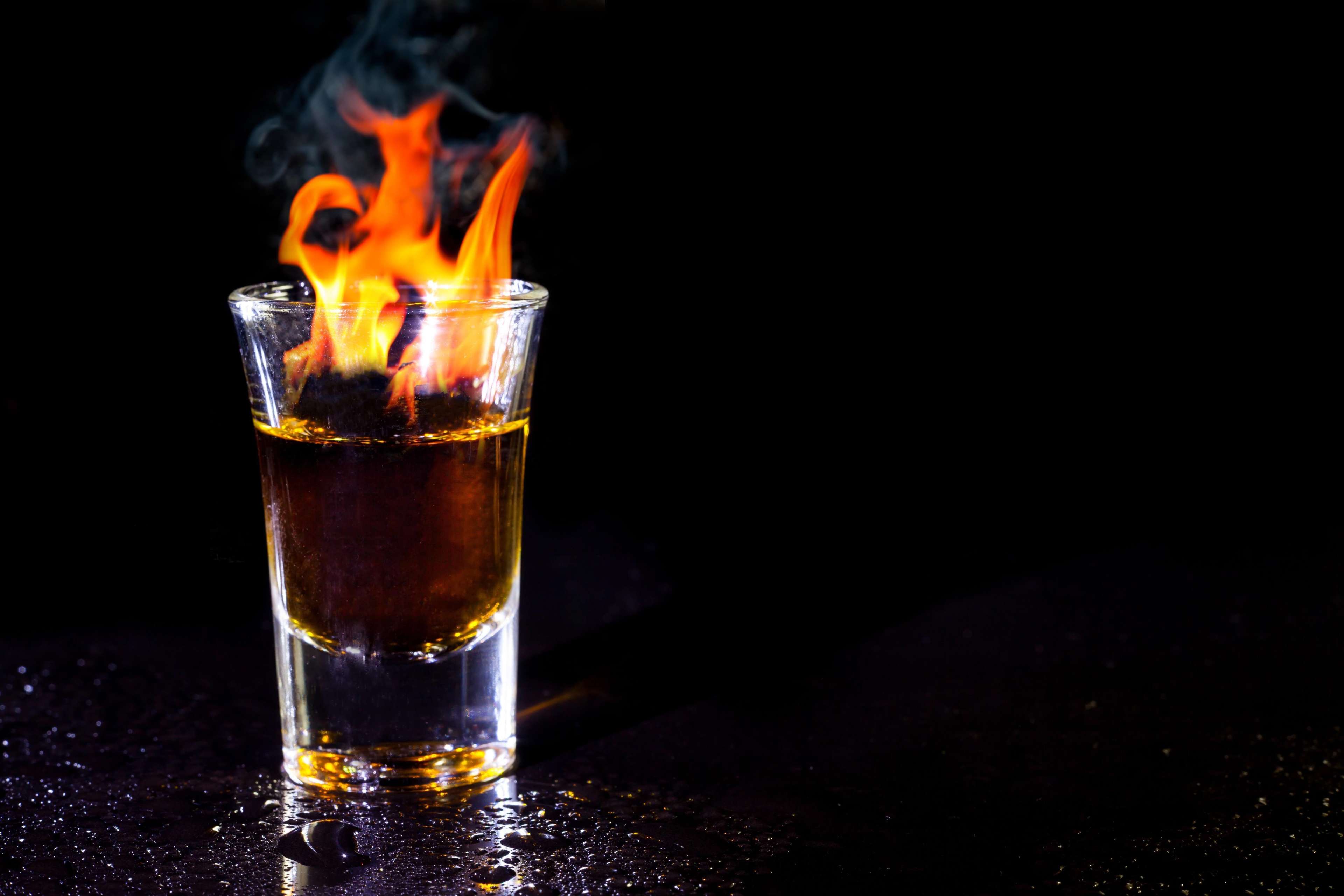 Hot alcoholic cocktail burning in shot glass