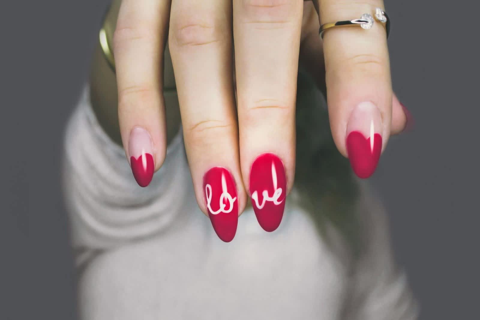 Mani with two red nails that spell “lo” & “ve” in the middle & three clear nails with red heart-shaped tips