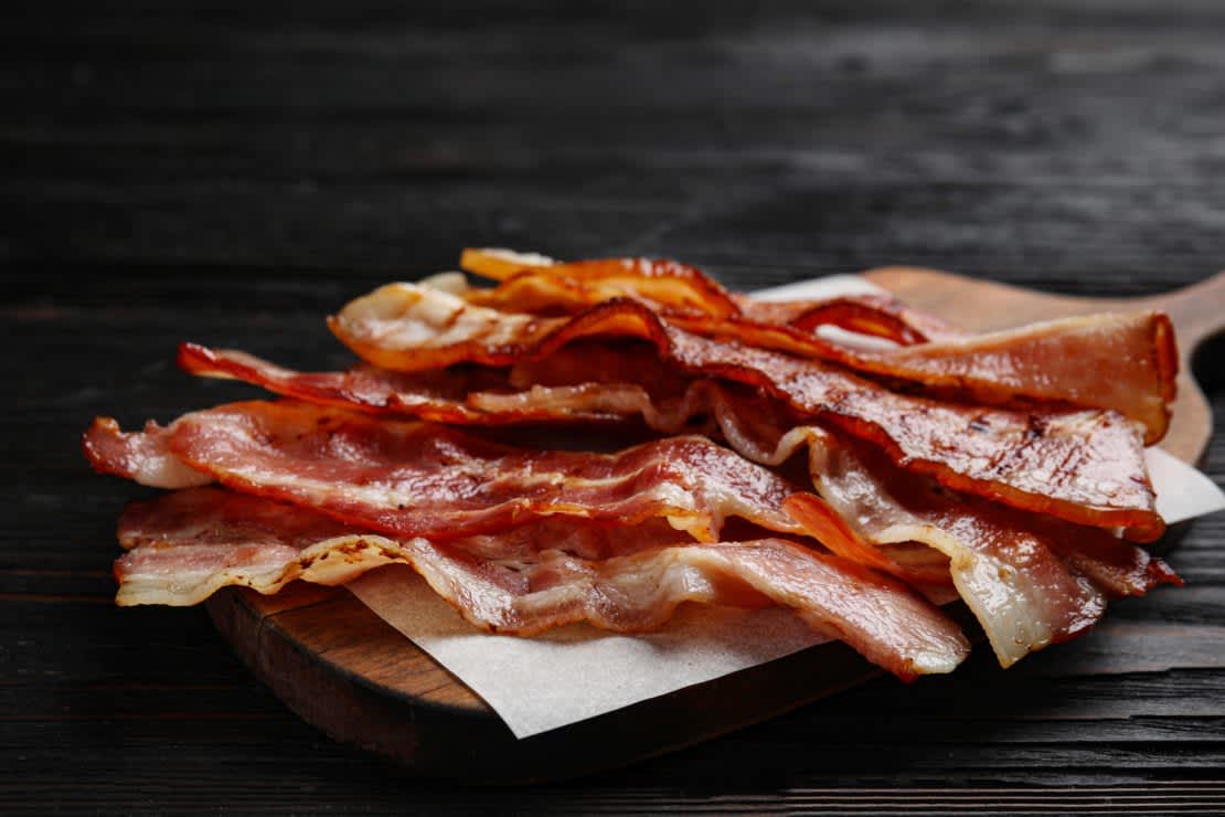 Slices of tasty fried bacon on black wooden table closeup