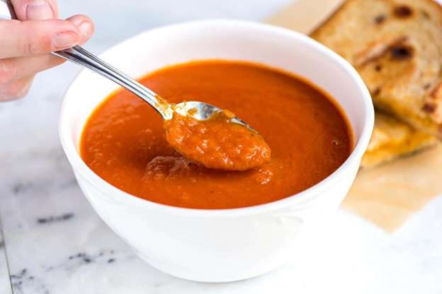 A bowl of tomato soup and spoon with tomato soup on it