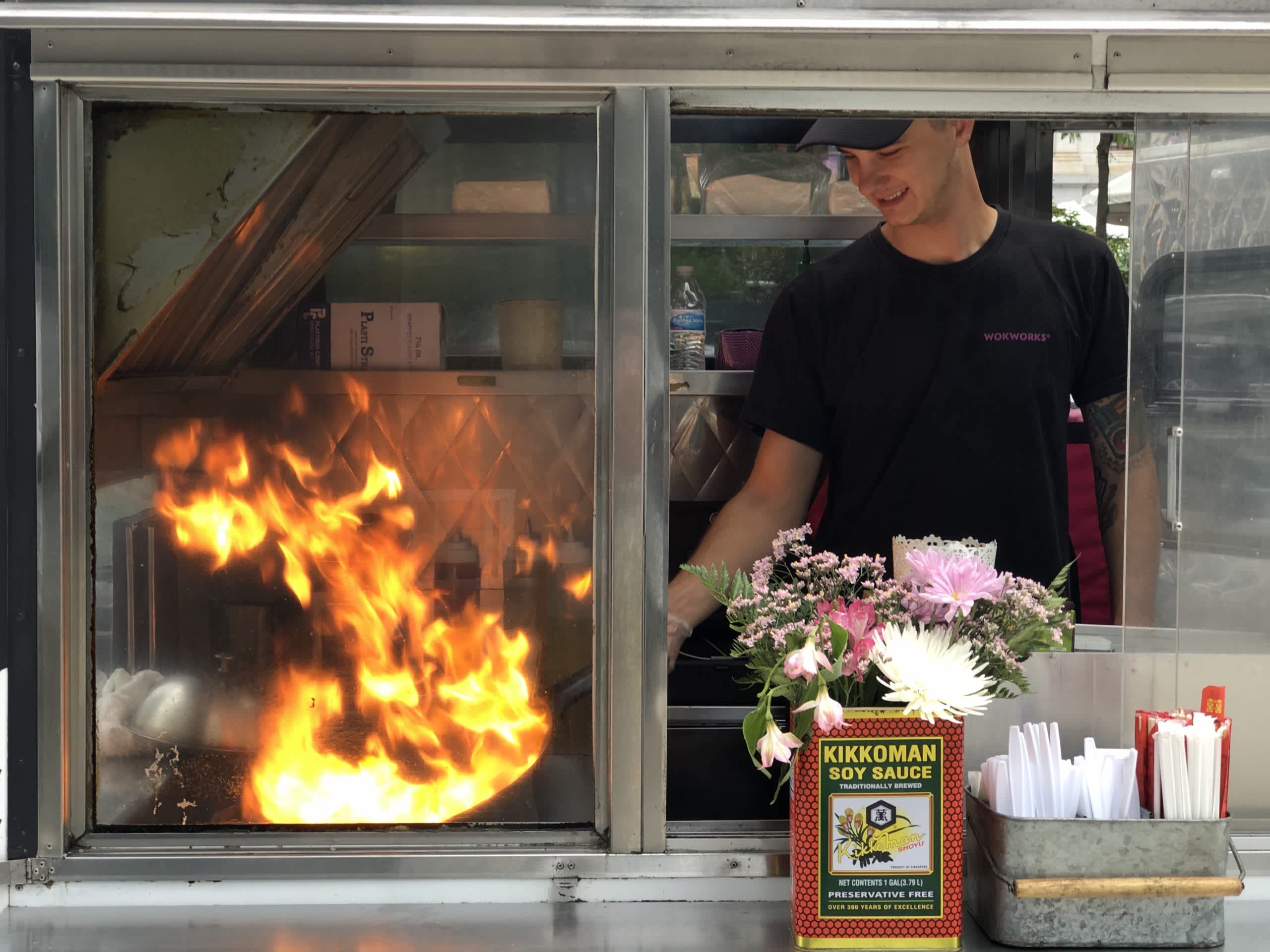Employee inside Wokworks food truck in Philadelphia frying Asian-fusion food in a flaming wok