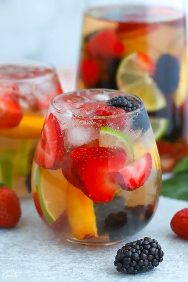 A glass of white sangria on a table surrounded by fruit