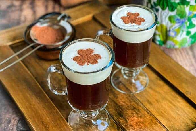 2 non-alcoholic Irish coffees with cocoa shamrocks latte art in glass mugs on wooden tray