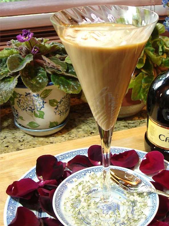 An Irish coffee in a champagne glass on a plate with flower petals