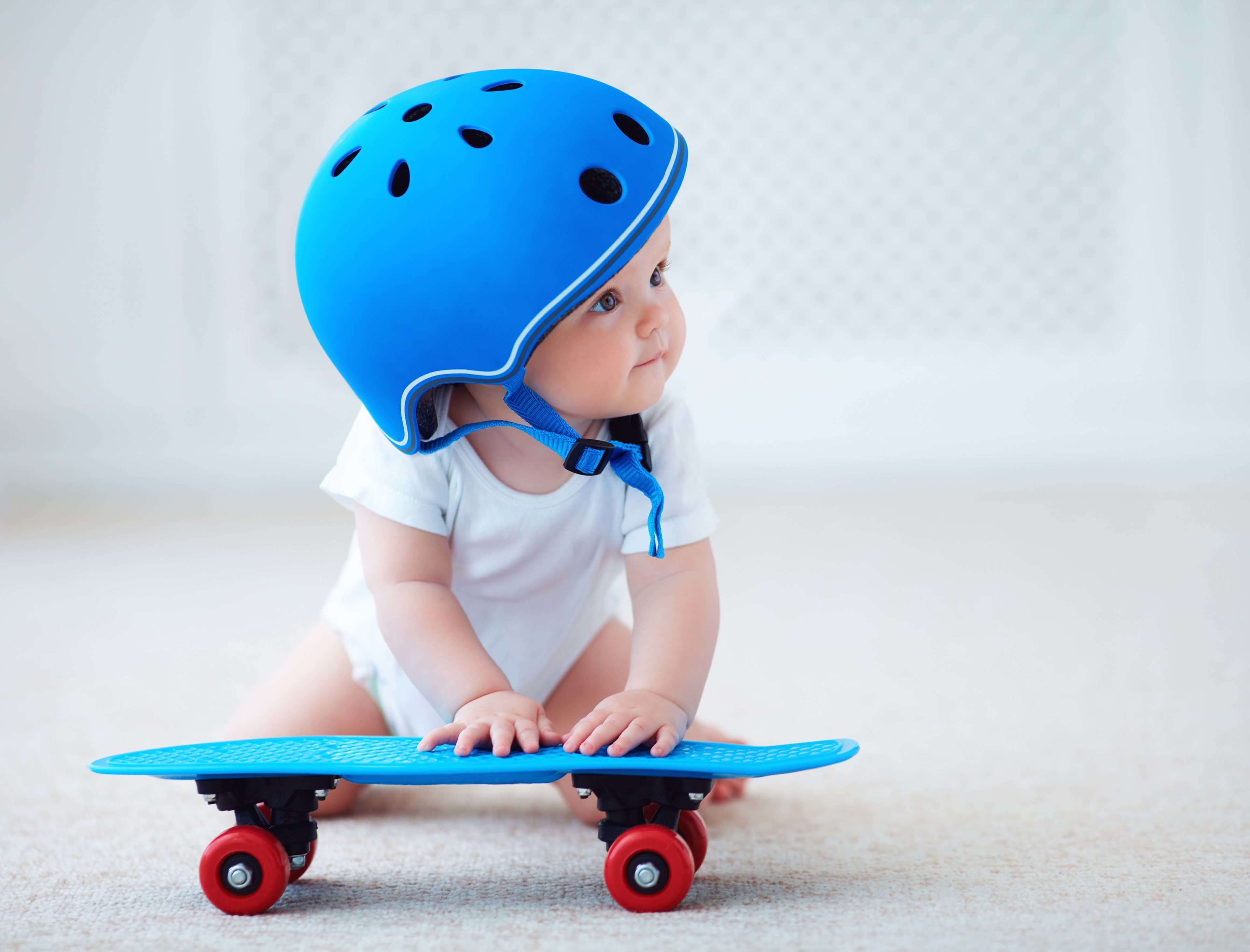 Cute infant baby girl in protective helmet outfit ready to ride skateboard