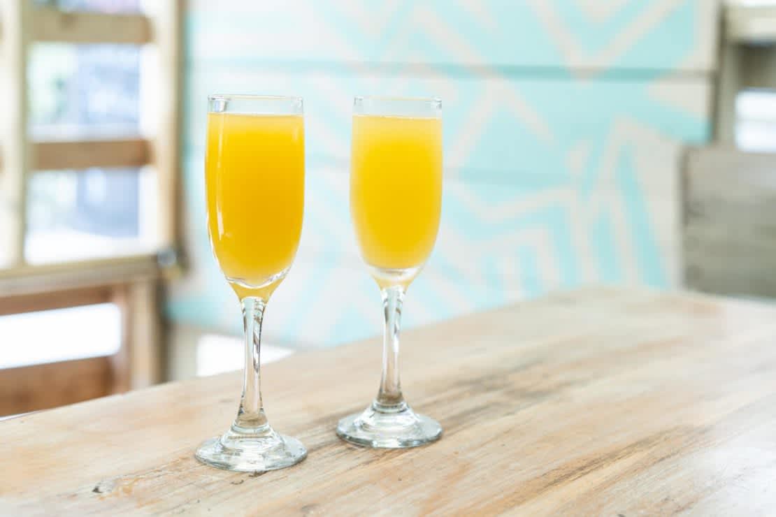 Two Champagne glasses filled with orange juice mimosas