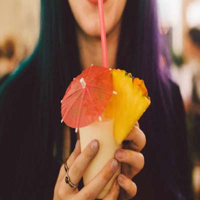 Girl drinking a Pina Colada out of a glass with pineapple and a drink umbrella.