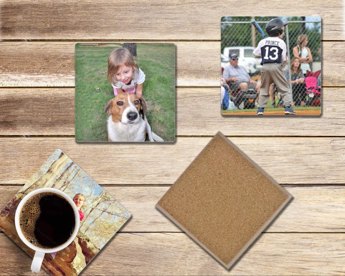 Four customized photo coasters on top of a wooden table with a cup of coffee