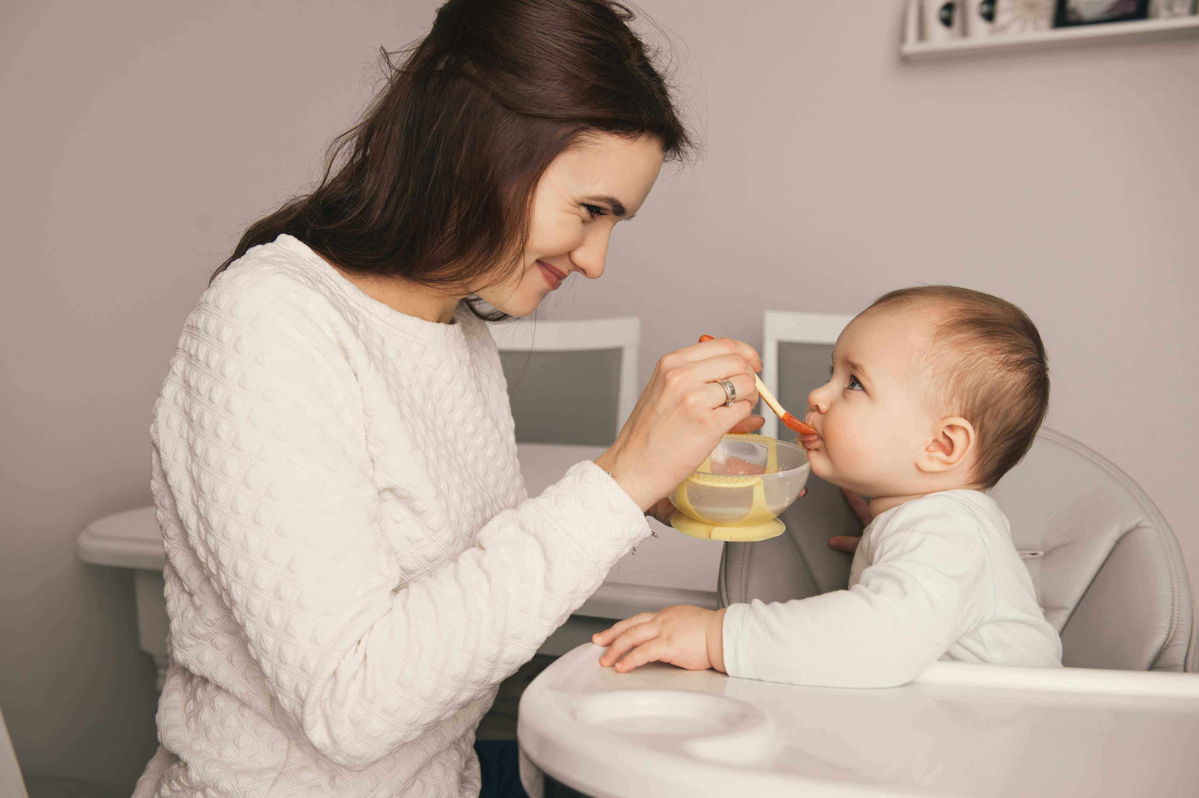 Mom feeding her nine month old baby girl with a spoon at home 