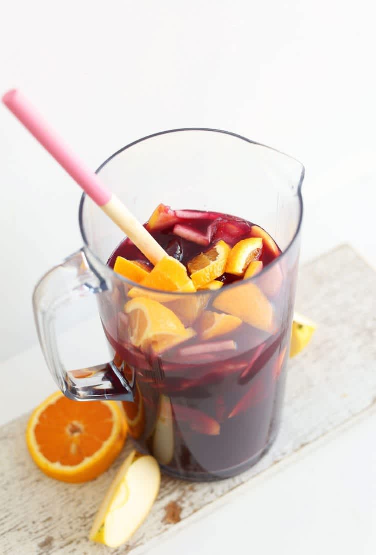A pitcher of red sangria on a table next to an orange