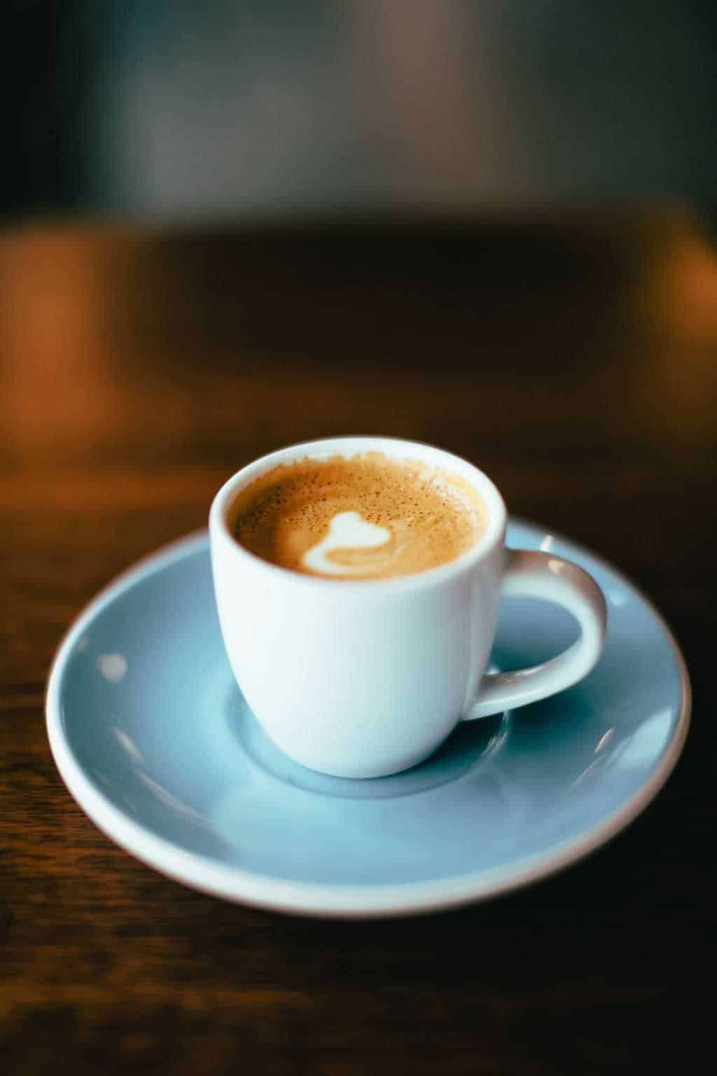 Macchiato with white milk heart latte art in small espresso cup on saucer