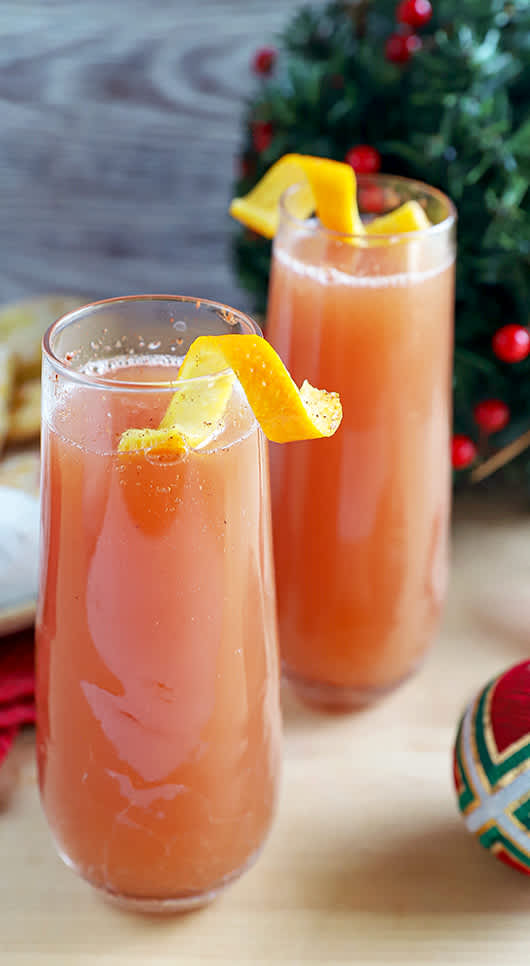 2 sparkling apple cranberry mimosa mocktails in stemless champagne flutes with orange twists