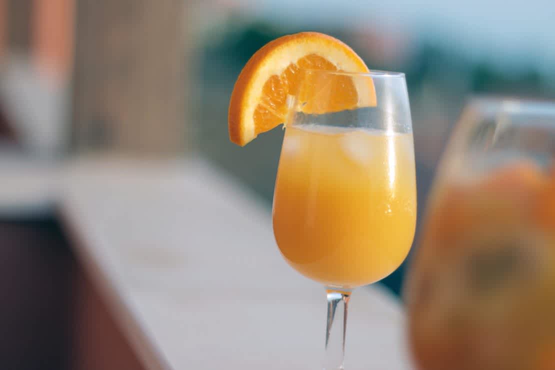 An orange juice mimosa in a champagne glass garnished with an orange wedge