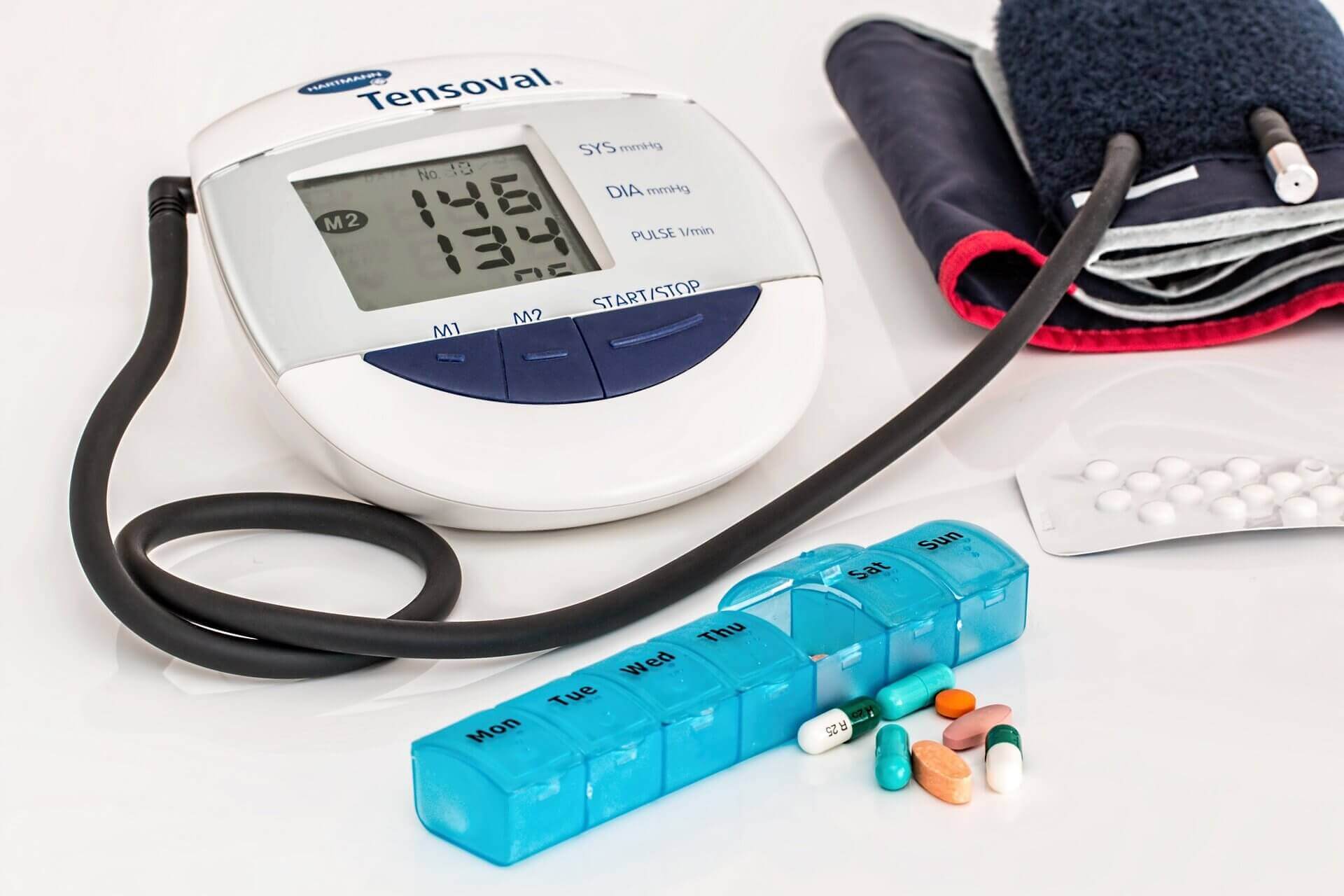 Digital blood pressure monitor, pill organizer and bendryl tablets on white background