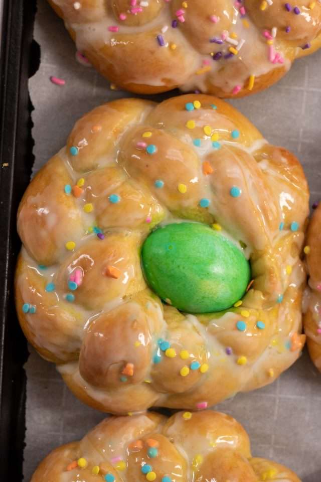 Loaf of Italian Easter bread with a sweet glaze, sprinkles and a dyed hard-boiled egg in the middle.