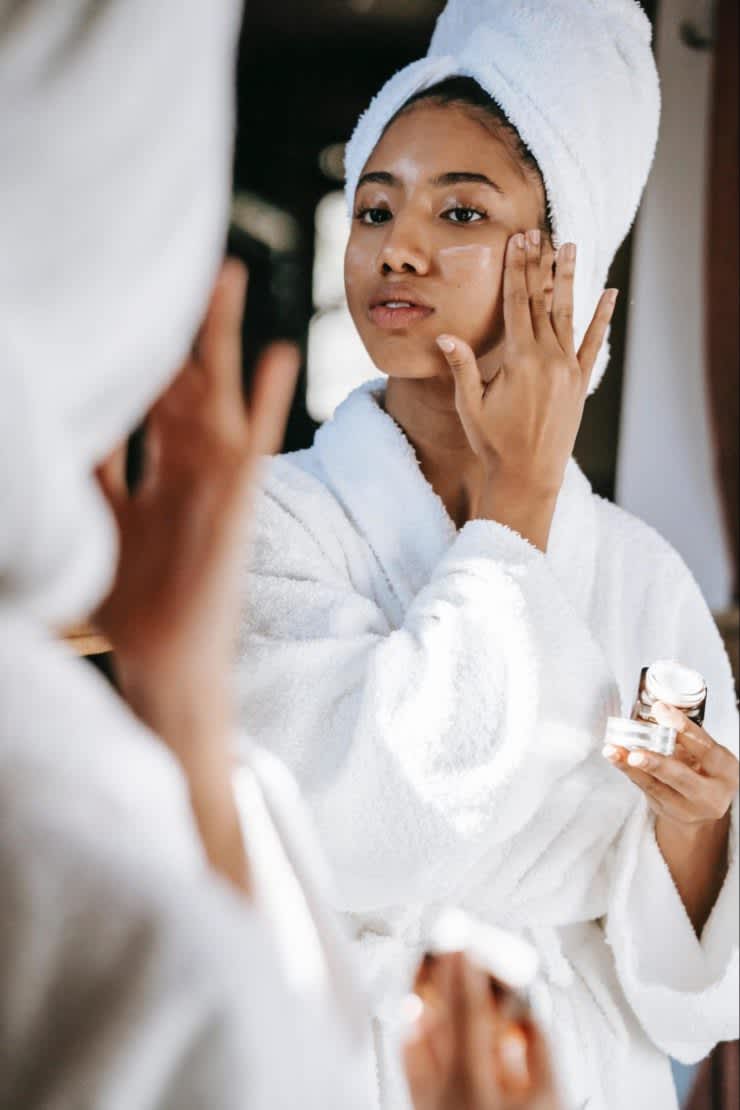Black woman in robe and towel applying skin cream to her face