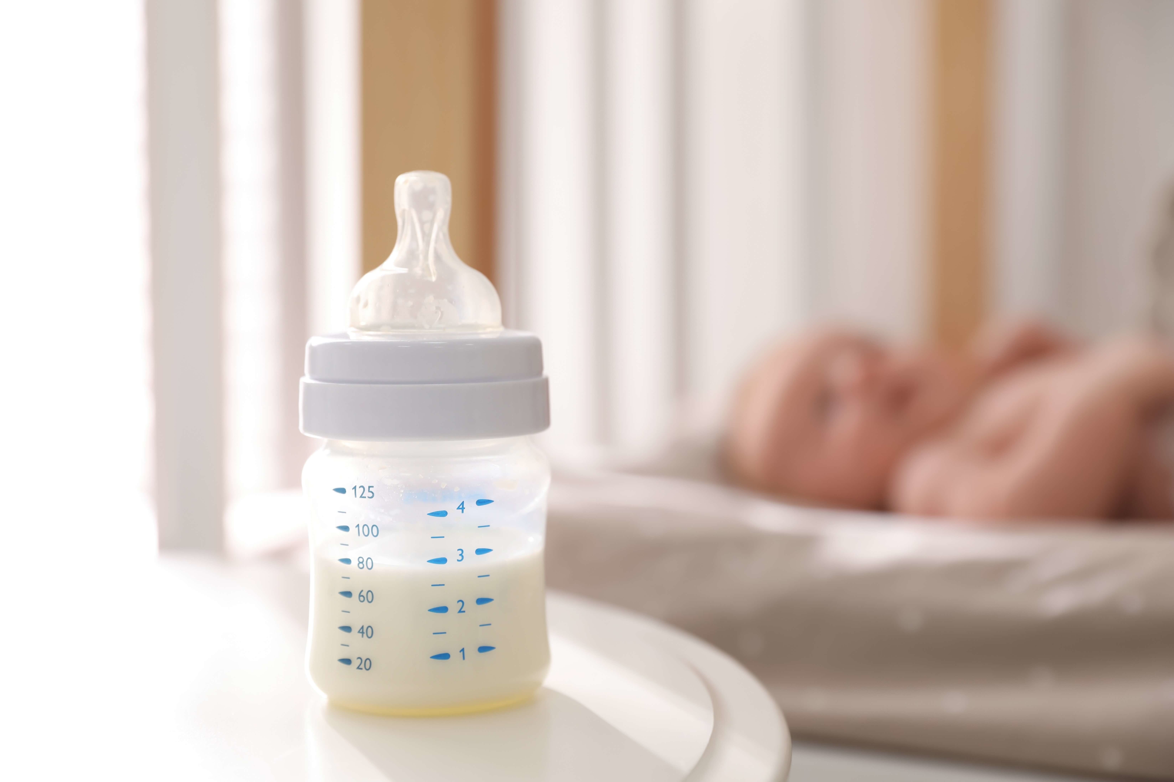 Focus on bottle with milk and four month old baby sleeping on background