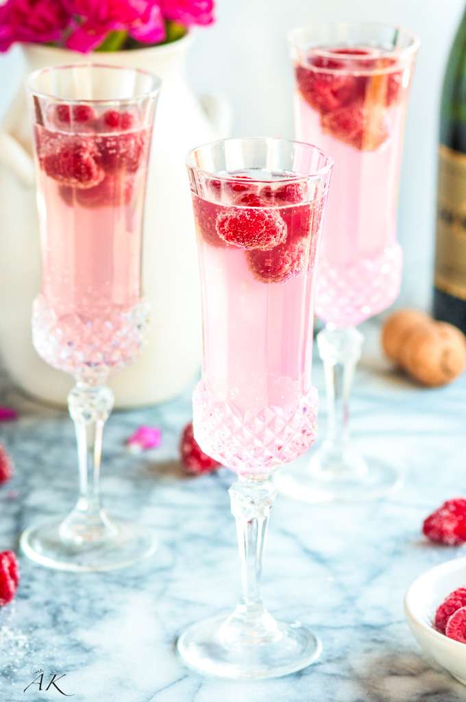 3 pastel pink mimosas in vintage stemmed cocktail glasses garnished with raspberries.