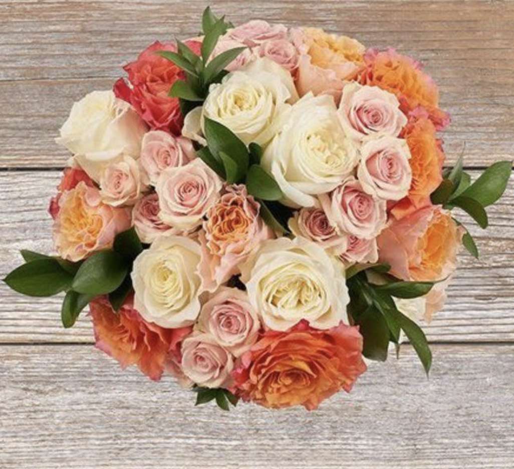 Arrangement of pink, red, orange and white roses on top of a wooden table