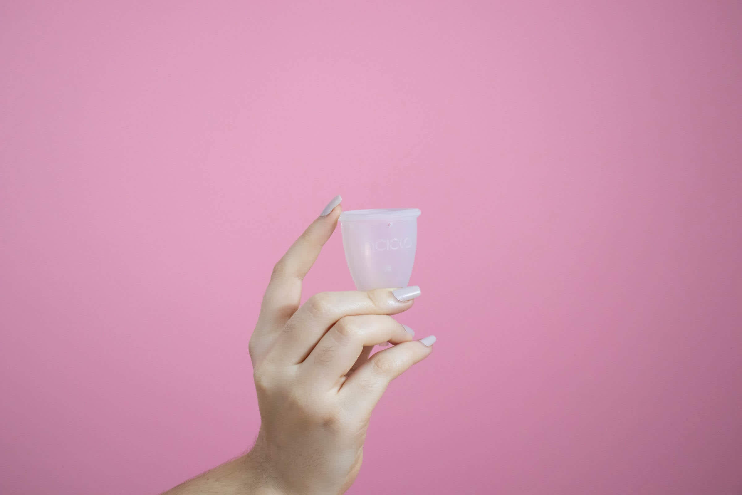 Person's hand holding clear menstrual cup with pink background