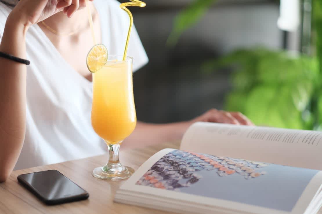 A woman reading a book and sipping on a mimosa with a long straw