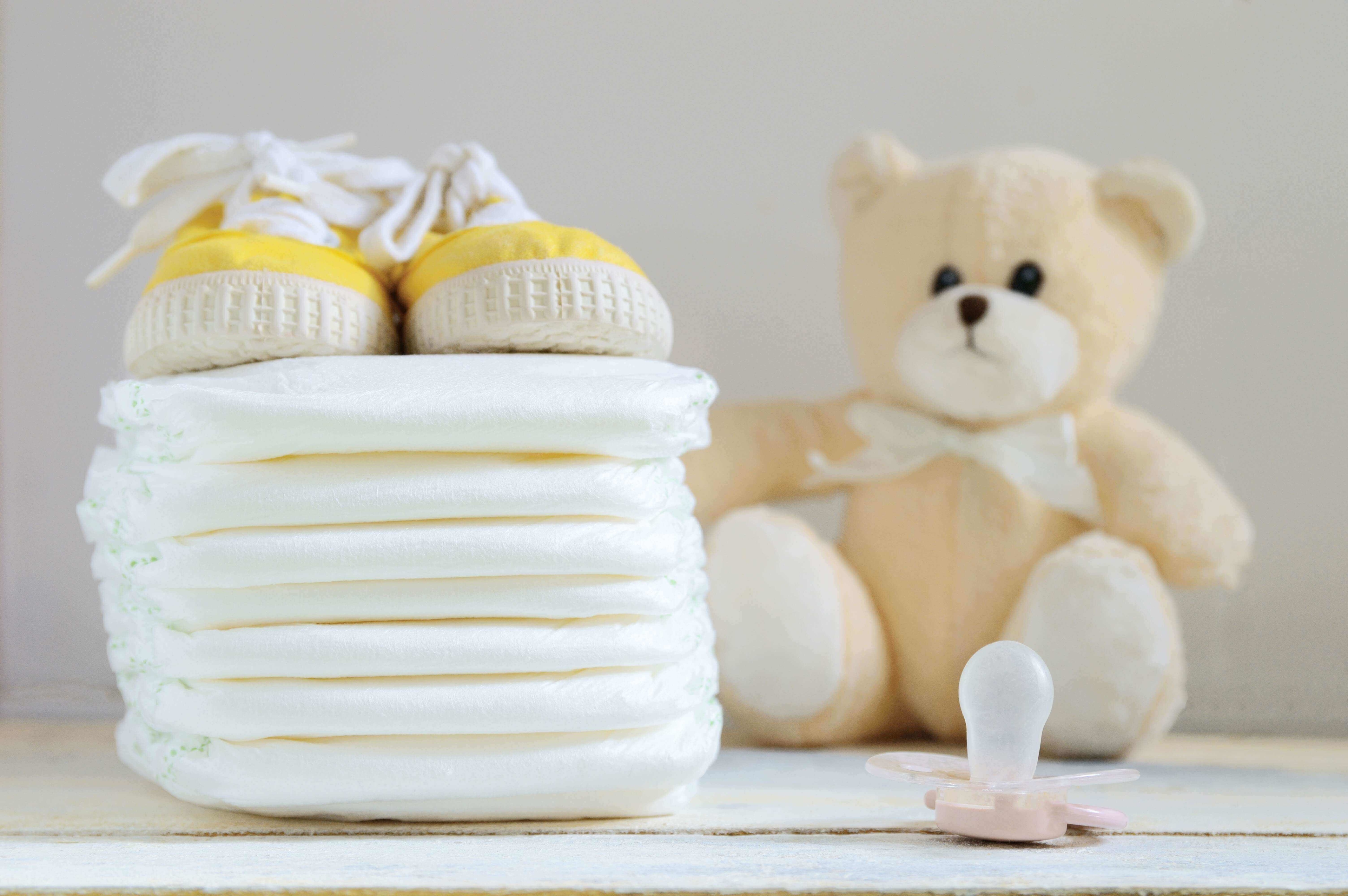 Baby diapers, yellow baby sneakers, a pacifier and a teddy bear