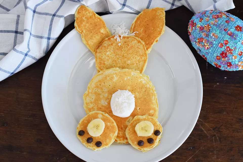 Six pancakes of various shapes and sizes assembled in the shape of a bunny. Includes banana and chocolate chip toes, and a marshmallow tail.