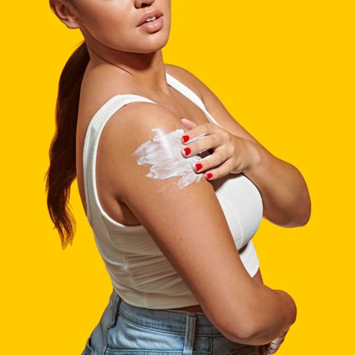 Woman in white tank-top putting some cream on her arm