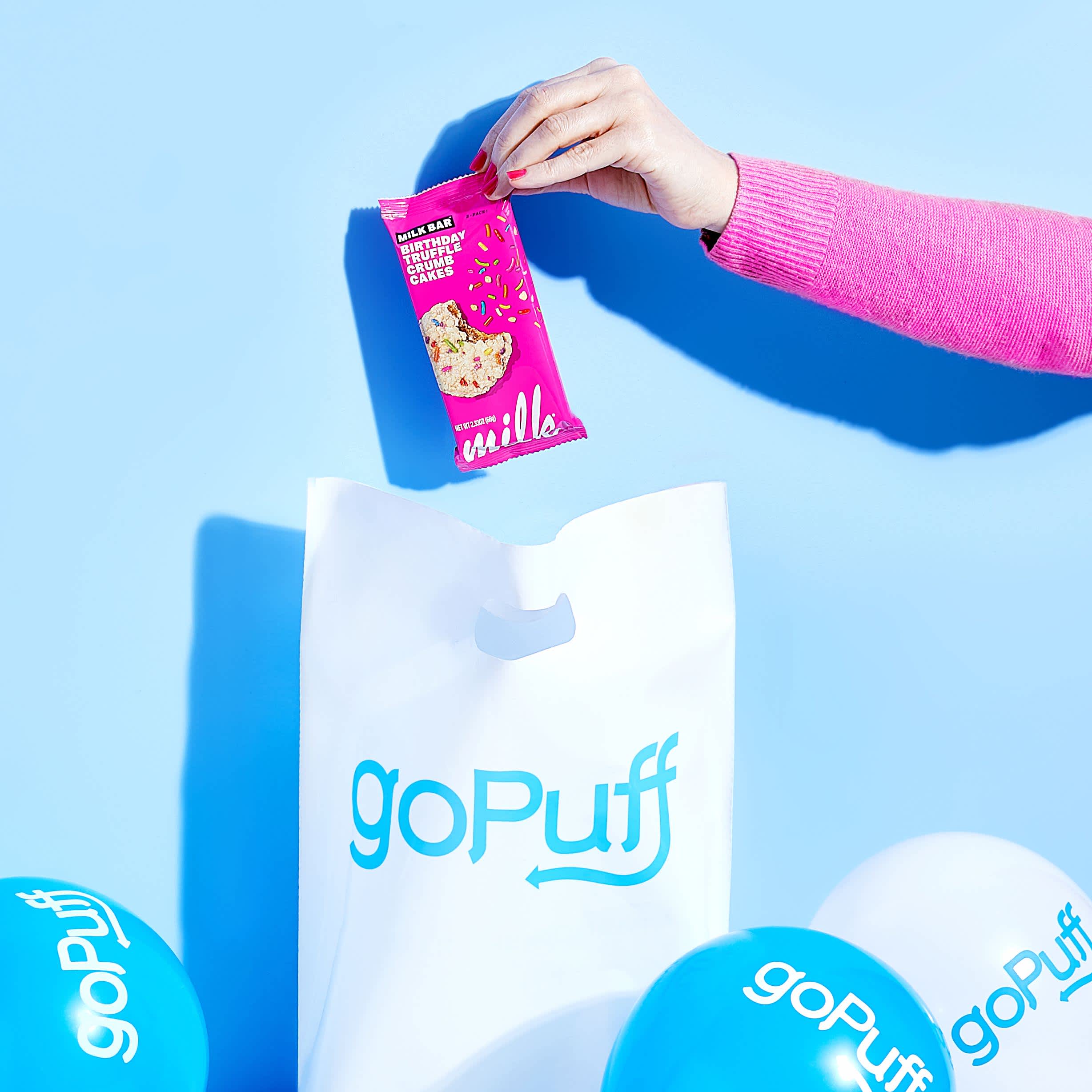 A Milk Bar being placed into a Gopuff bag surrounded by balloons for the 7th Gopuff anniversary