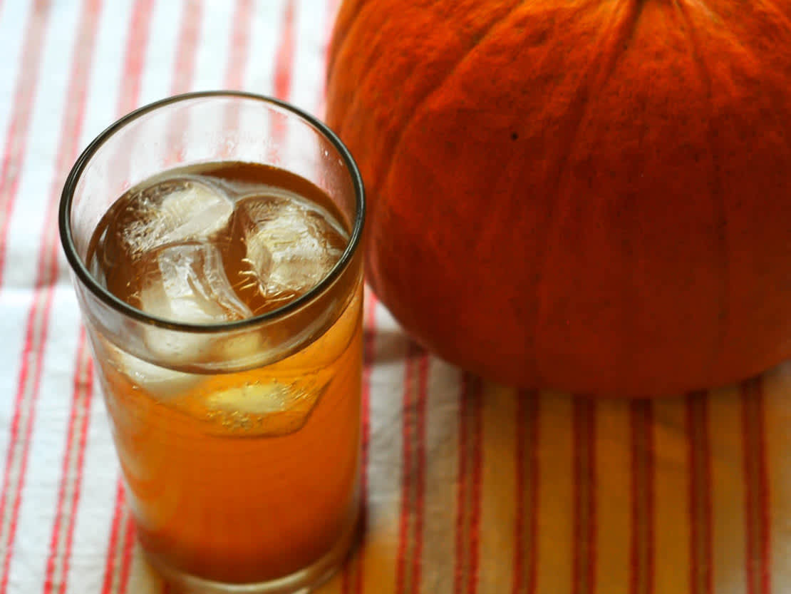 Glass with pumpkin shrub drink next to pumpkin