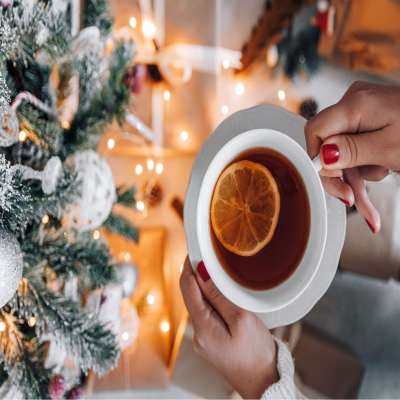 Woman holding cup of tea with lemon in it near a Christmas tree.