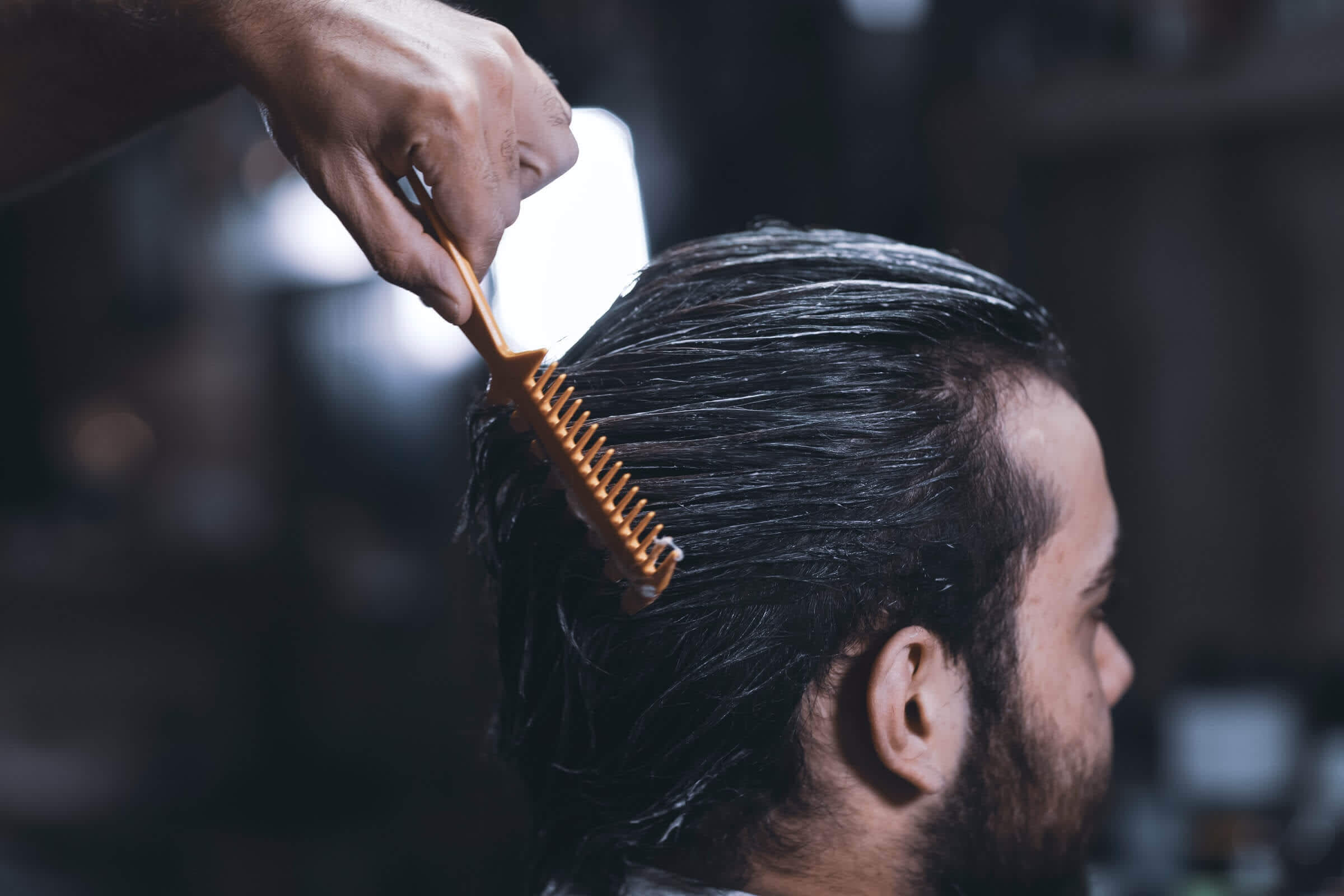 Barber applying shampoo for man's hair care and brushing with comb at barbershop