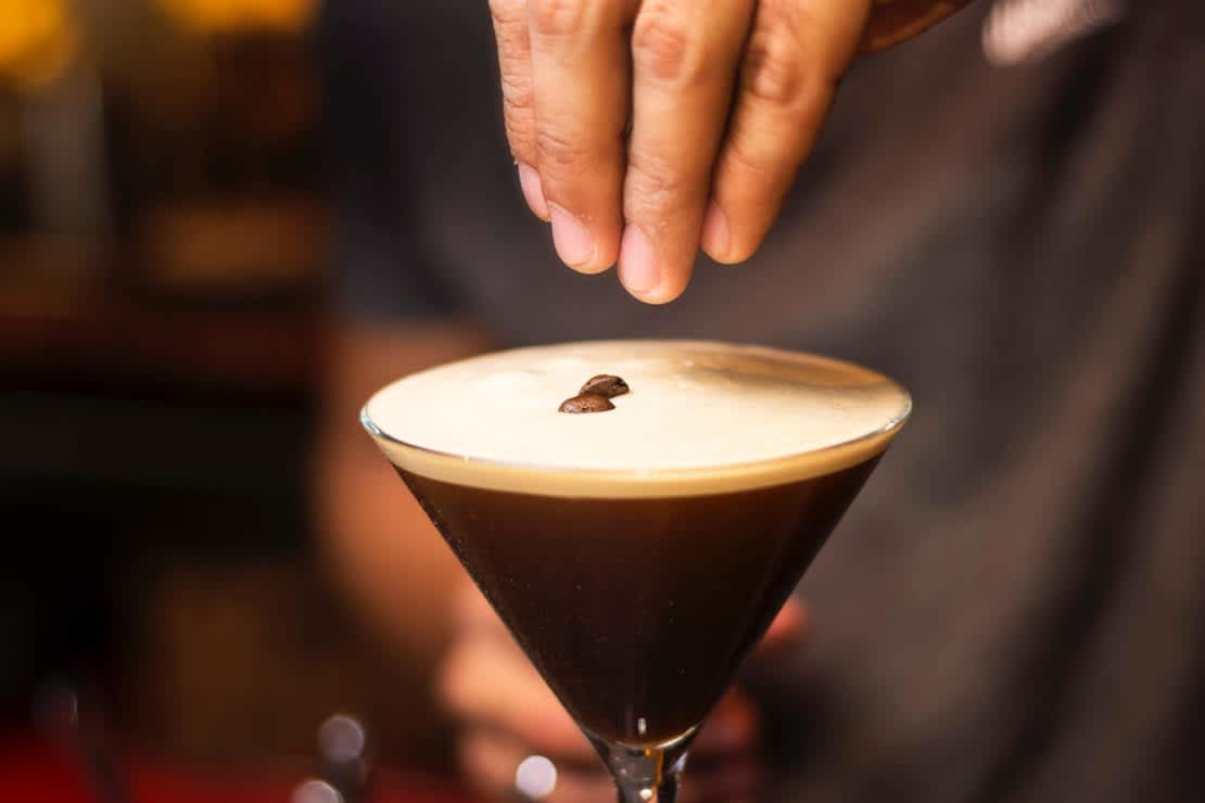 A bartender garnishing an espresso martini with coffee beans
