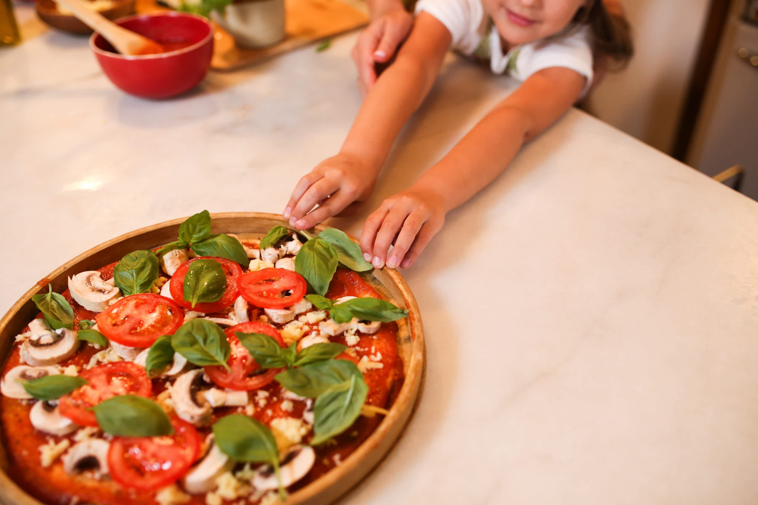 A child reaching for a homemade pizza