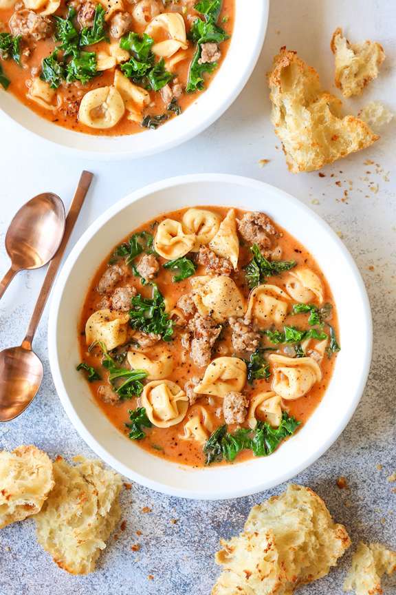 Bowls of tortellini soup with spoons and crusty bread