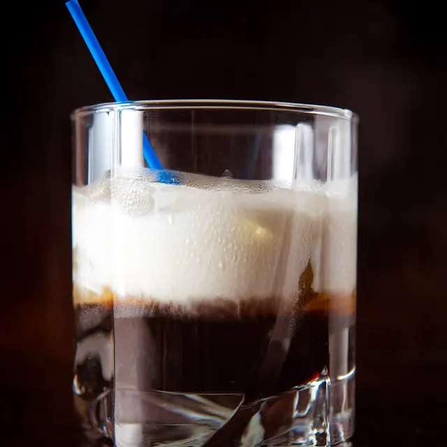 A Dirty White Russian cocktail in highball glass with a blue straw