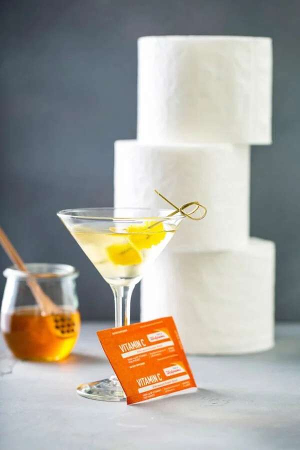 The quarantini cocktail with a vitamin C packet, honey and three rolls of toilet paper in the background