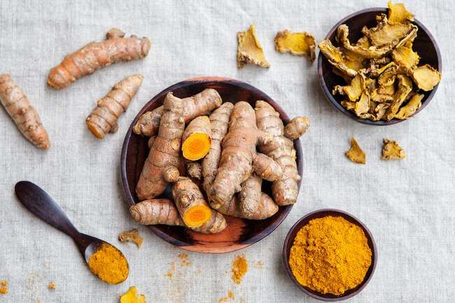 Turmeric root in a bowl and ground turmeric in another bowl